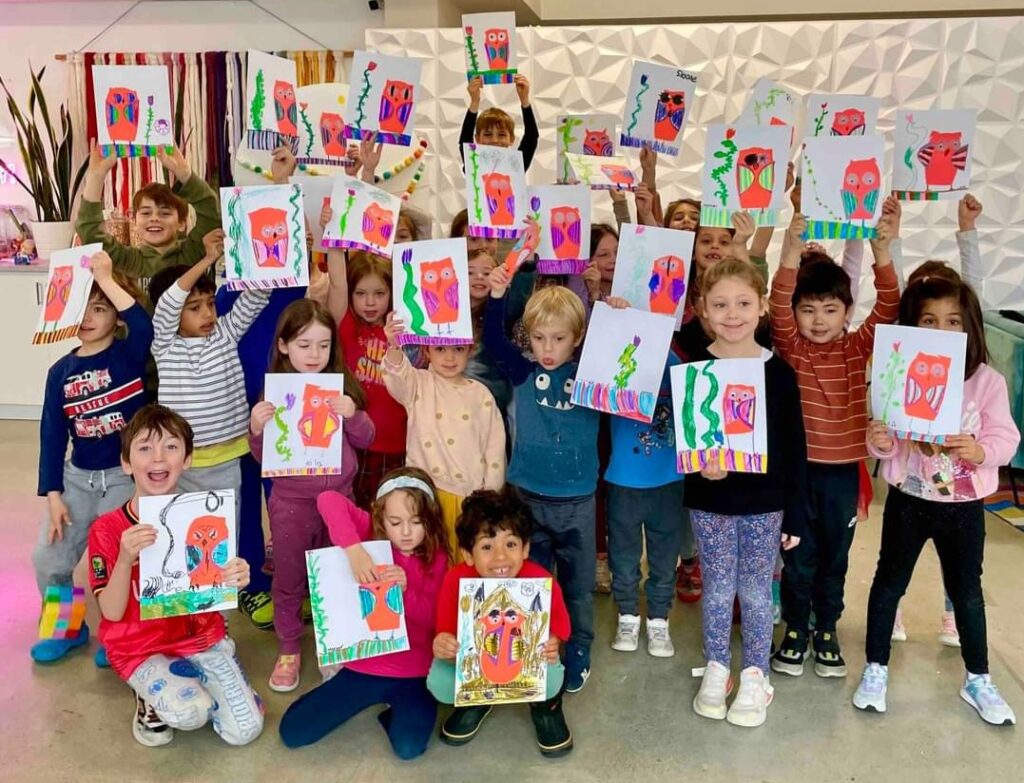 A large group of smiling children holding up their artwork